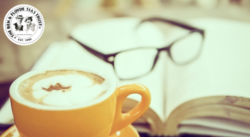 Image of yellow mug with coffee and and an open book with reading glasses on top in the background
