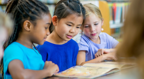 Image of three young girls looking at a book at the library